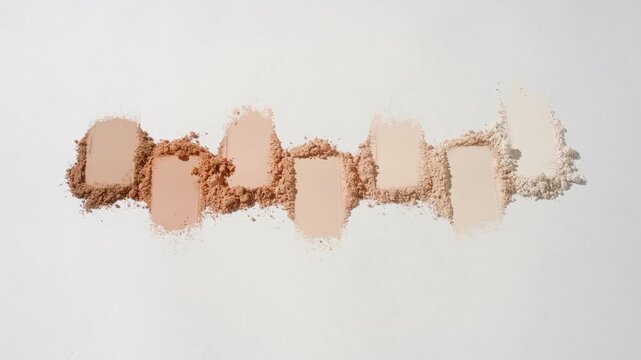 Vertical arc slow motion shot of water flowing over seven beige to brown powder smears on a muted grey background
