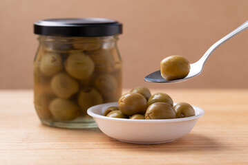 Pickled olives, Pitted green olives in glass jar and bowl with spoon on wooden background