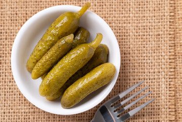 Pickled cucumber or Gherkin pickle in a bowl with fork on brown background, Top view