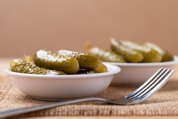 Pickled cucumber or Gherkin pickle in a bowl with fork on brown background