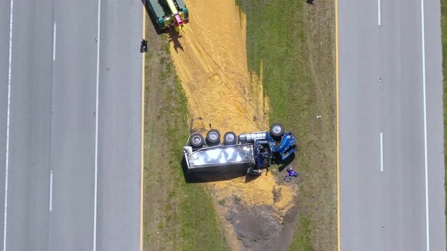 Aerial view of traffic accident with overturned truck on highway road median being rescued by tow truck crane.