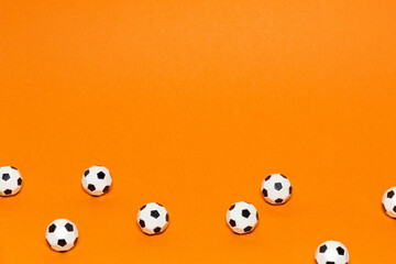 Mini soccer balls scattered on an orange background, visual pattern of consistency and discipline