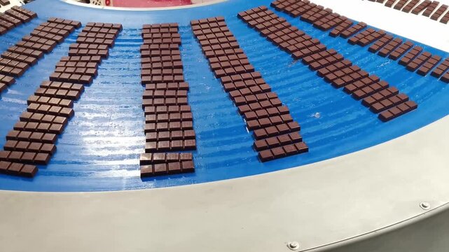 A close-up shot of chocolate bars moving in neat rows along a bright blue conveyor belt in a food production facility.