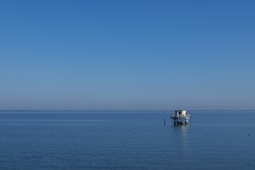 Small white observation hut standing in the calm blue sea / Minimalist seascape with copy space