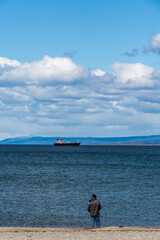 Outlook over the magellan strait, showing a fisherman and a big ship.