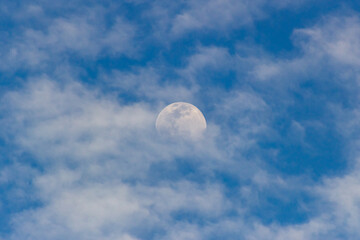 Moon in the blue sky with white clouds. Blue sky background.