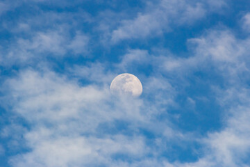 Moon in the blue sky with white clouds. Blue sky background.