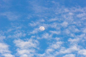 Moon in the blue sky with white clouds. Blue sky background.