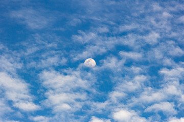 Moon in the blue sky with white clouds. Blue sky background.