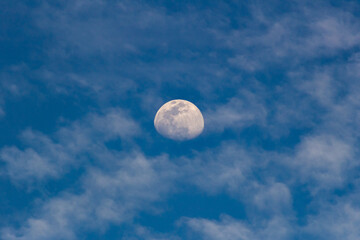 Moon in the blue sky with white clouds. Blue sky background.