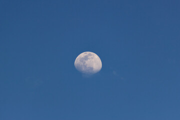 Moon in the blue sky with white clouds. Blue sky background.