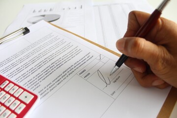 An inspection executive giving signature on a inspection report result either it is passed or failed. Business improvement concept. Soft focus. Working paper with documentation, calculator, pen and ch
