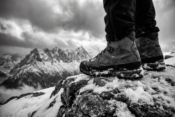 Close up of hiker boots standing on snowy mountain peak with dramatic clouds in background