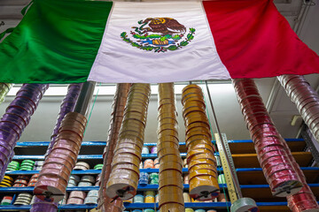 Mexican national flag hanging with colorful fabric ribbon spools on display in a haberdashery store