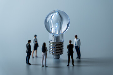 Miniature business people standing around a light bulb. Teamwork, brainstorming, ideas, problem solving concept.