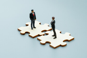 Miniature business figures stand on interlocking puzzle pieces. Corporate partnership, teamwork, strategic collaboration concept.