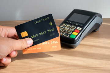 Hand holding yellow and black credit cards in front of an electronic EDC terminal on a wooden desk. Perfect for fintech, payment systems, ecommerce, business finance, banking services, technology