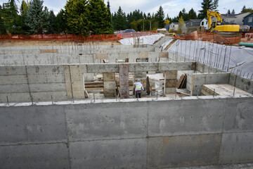 Naklejka premium Construction worker using hammer to remove wood form from pored cement wall in a large stormwater retention system tank on a construction job site, sunny fall day 
