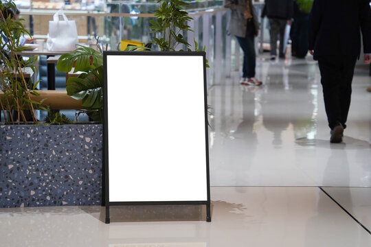 Blank white outdoor advertising stand sandwich board mock up template. Clear street signage board placed by an indoors dinning area of a restaurant in shopping mall.