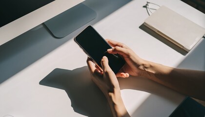 Person holding a smartphone on a desk with a computer monitor and notebook.