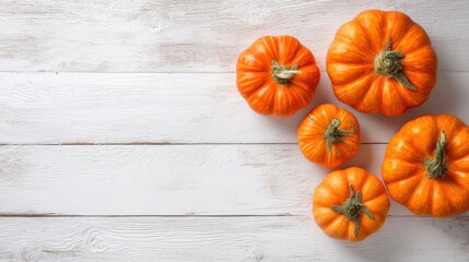 Five orange pumpkins of different sizes sit on a white wooden surface. The pumpkins are freshly harvested and show bright colors. This image represents the autumn harvest season.