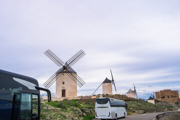 Tourist coaches parked along the roadside near the iconic windmills and medieval castle on the hilltop of Consuegra along the Don Quixote Route in spring.