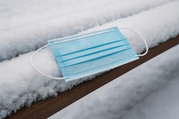 Disposable face mask on a snowy bench