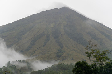 A real, unedited view of the majestic Mount Inerie volcano peak surrounded by natural mist and tropical forest in Flores, East Nusa Tenggara.
