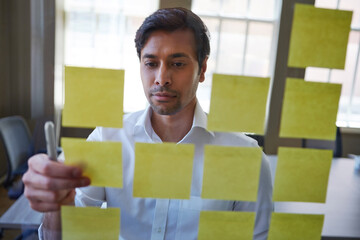 Corporate, man and reading sticky note on glass for planning, schedule update and reminder. Male person, review and brainstorming with strategy, moodboard timeline and information for proposal offer
