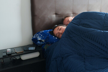 Young couple sleeping soundly in bed with an alarm clock set to 6:00 am