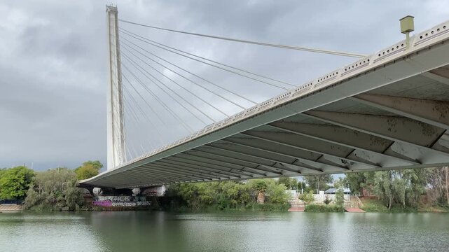 Low angle view beneath the Alamillo bridge reveals its steel deck, tall pylon and cable system above the green river
