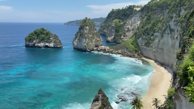 Aerial drone shot of dramatic limestone cliffs and turquoise ocean at Nusa Penida in Bali Indonesia showing sandy beach, clear water and scenic tropical coastline.