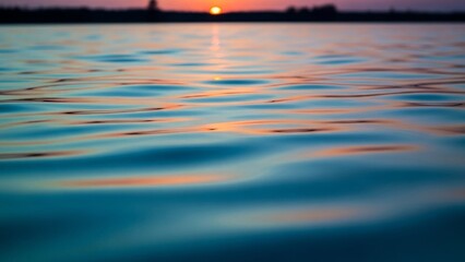 Close-up view of tranquil blue water ripples reflecting the warm colors of a distant sunset.