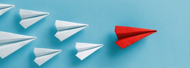 Red paper airplane leads white ones on light blue background, overhead shot