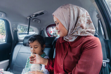 An Indonesian Muslim woman feeding foods to her daughter in a car