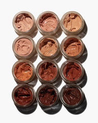 Variety of foundation makeup colors in glass jars on white background