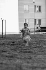Young girl with a teddy bear running joyfully across a grassy field, wearing a light dress and sneakers, capturing the essence of childhood playfulness and freedom