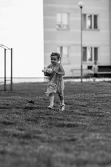 Young girl with a teddy bear running joyfully across a grassy field, wearing a light dress and sneakers, capturing the essence of childhood playfulness and freedom