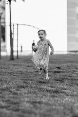 Young girl with a teddy bear running joyfully across a grassy field, wearing a light dress and sneakers, capturing the essence of childhood playfulness and freedom