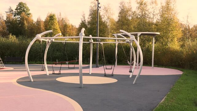 Modern children playground with swings and creative play equipment featuring rubber safety flooring and rounded edges integrated into green natural environment for outdoor play learning and enjoyment