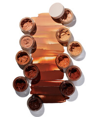 Variety of foundation makeup colors in jars with swatches on white