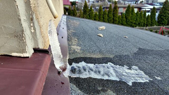 Frozen drainage pipe on house roof with ice accumulation near wall after winter frost period