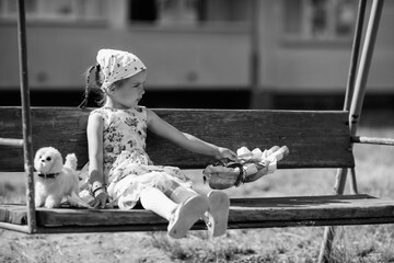 Young girl with braided hair wearing a patterned dress and headscarf is playing with toys on a grassy field, surrounded by colorful play items and a joyful atmosphere