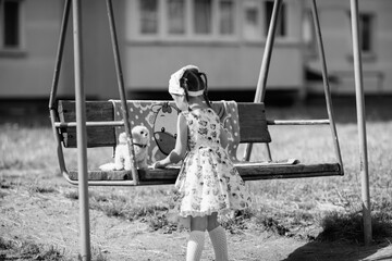 Young girl with braided hair wearing a patterned dress and headscarf is playing with toys on a grassy field, surrounded by colorful play items and a joyful atmosphere