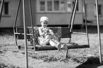 Young girl with braided hair wearing a patterned dress and headscarf is playing with toys on a grassy field, surrounded by colorful play items and a joyful atmosphere