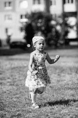 Young girl with braided hair wearing a patterned dress and headscarf is playing with toys on a grassy field, surrounded by colorful play items and a joyful atmosphere