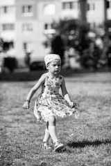 Young girl with braided hair wearing a patterned dress and headscarf is playing with toys on a grassy field, surrounded by colorful play items and a joyful atmosphere
