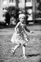 Young girl with braided hair wearing a patterned dress and headscarf is playing with toys on a grassy field, surrounded by colorful play items and a joyful atmosphere