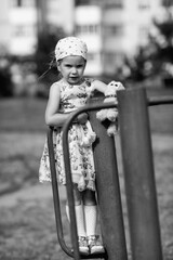 Young girl with braided hair wearing a patterned dress and headscarf is playing with toys on a grassy field, surrounded by colorful play items and a joyful atmosphere