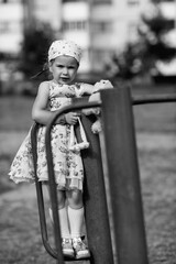 Young girl with braided hair wearing a patterned dress and headscarf is playing with toys on a grassy field, surrounded by colorful play items and a joyful atmosphere